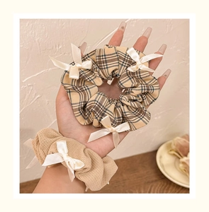 Detail of vintage plaid and beige scrunchies with white satin bows on a soft backdrop