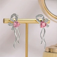 Detail of silver bow earrings with pink heart gemstones on a golden display stand