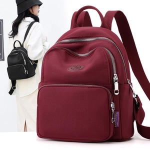 Detail view of burgundy nylon backpack with multiple zipper compartments and brand tag