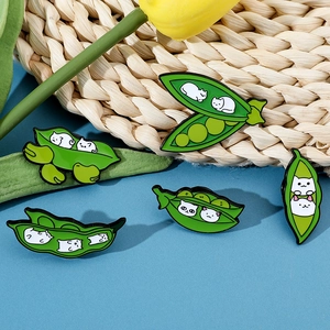 Detailed close-up of five cute cat-faced pea pod enamel pins on a natural woven mat