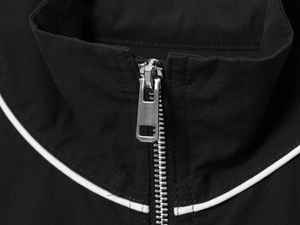 Macro detail of silver metal zipper and white contrast piping on black nylon bomber jacket