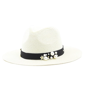 Detail of white straw fedora hat featuring black band with pearl and floral accents