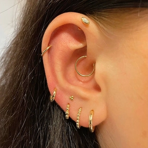 Close-up of minimalist gold earring set with studs and hoops on a model's ear