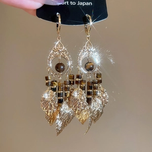 Detail of gold-plated geometric earrings with tiger eye stone and metal leaf tassels