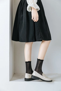 Close-up of black lace mesh socks paired with beige loafers and a pleated skirt