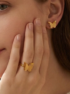 Close-up of matte gold butterfly stud earrings and matching ring on a model