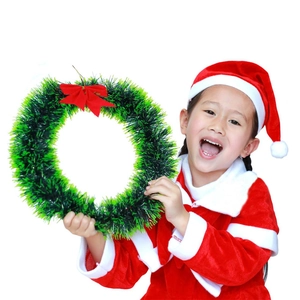 A young girl in a Christmas dress holding a green wreath with a bright red bow decoration