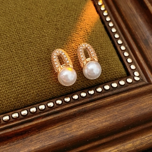 Gros plan de boucles d'oreilles dorées en U avec zircons et perles sur tissu