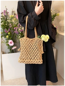 Detail of beige hollow woven tote bag with tassel accents on a model in nature setting