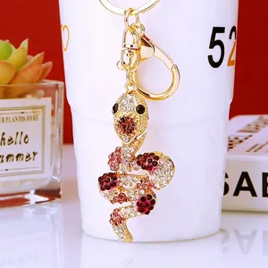 Golden snake keychain with sparkling red and white rhinestones on a white ceramic cup