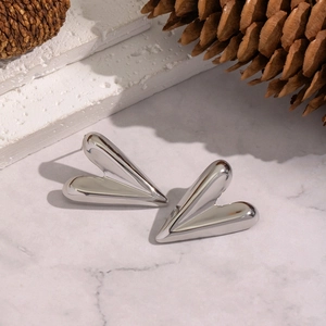 Macro detail of silver polished 3D heart stud earrings on decorative stone and pinecone