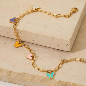 Detail of gold ankle chain with five colorful enamel butterfly charms on stone base