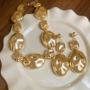 Golden oval link necklace and earring set displayed on a white textured ceramic tray