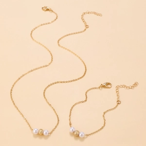 Dettaglio del set collana e bracciale con perle dorate su uno sfondo beige caldo