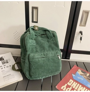 Detail eines grünen Cord-Rucksacks mit Tragegriff und Reißverschlussfach auf Metalloberfläche