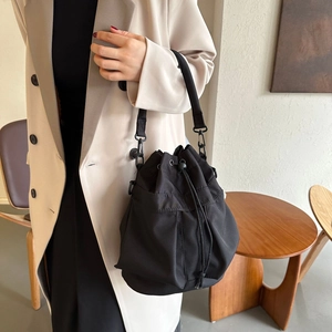 Vue détaillée du sac seau noir à cordon porté avec un manteau d'hiver beige chic