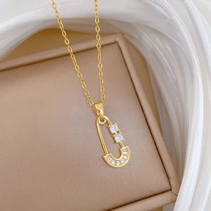 Detail of gold safety pin necklace with zircon stones on beige jewelry box