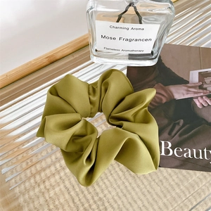 Chic olive green satin scrunchie displayed on textured glass with elegant decor