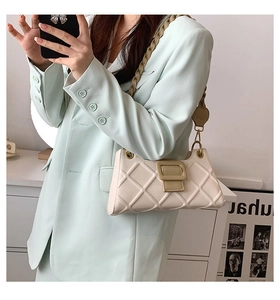 Detail of cream white quilted baguette bag with gold square buckle and chain strap