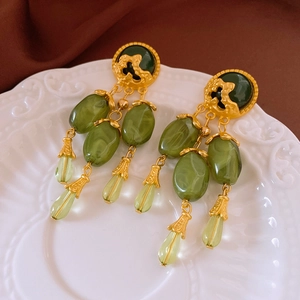 Detail view of vintage gold earrings with green gemstones on embossed ceramic plate