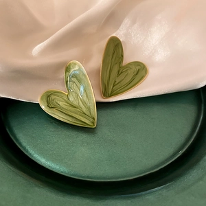 Close-up of green heart stud earrings with marble enamel texture and gold edges