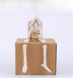 Detail of seated resin skeleton figurine with ivory finish and see no evil pose