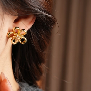 Close-up of golden hollow flower stud earring with zircon core worn by a model
