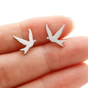 Minimalist silver swallow stud earrings with brushed metal finish on a finger for scale