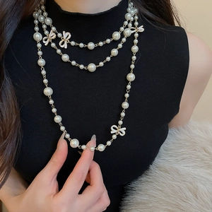 Close-up of triple-layered pearl necklace featuring white enamel bows on elegant black top