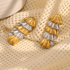 Macro detail of layered gold and silver shell-shaped earrings on textured fabric