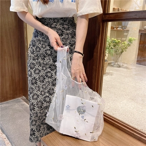 Detail of white mesh tote bag with purple flower embroidery held by a model