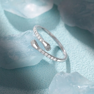 Macro view of S925 silver hugging hands ring with sparkling zircon stones on light blue background