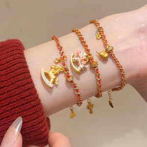 Détail de bracelets en corde rouge plaqués or 24K avec breloques de cheval et gourde