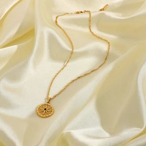 Gold starburst compass pendant necklace with water wave chain on beige silk fabric