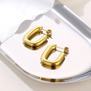 Minimalist gold U-shaped stud earrings in polished stainless steel on a silver tray