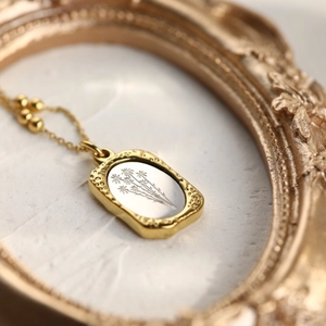 Close-up of vintage 18K gold rose pendant with silver floral engraving on a beaded chain
