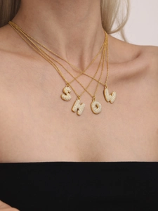 Close-up of four 18k gold necklaces with sparkling zircon-studded alphabet pendants