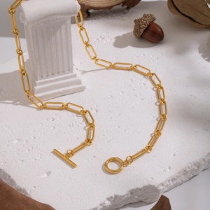 Detail of golden paperclip chain necklace with toggle clasp on textured stone