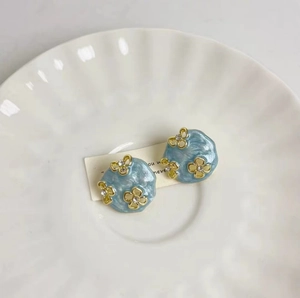 Détail de boucles d'oreilles fleur en émail bleu avec motif doré et petits strass