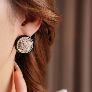 Close-up of model wearing round silver earrings with a black border and textured design