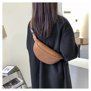 Brown leather crossbody chest bag shown on model in a cozy minimalist cafe setting