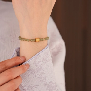 Close-up of a green jade bead bracelet with a gold lucky bead on a model's wrist