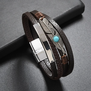 Macro detail of braided leather bracelet featuring a silver feather charm and turquoise bead