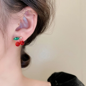 Close-up of cherry stud earrings with red beads and rhinestone-inlaid green leaves on model