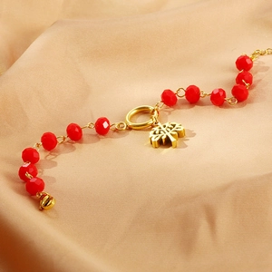 Detailed view of red faceted crystal bead bracelet with gold Tree of Life charm on silk