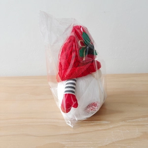 Detail of Christmas gnome with red knit hat and heart gloves in clear polybag packaging