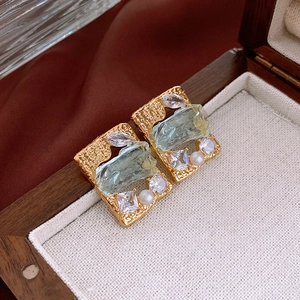 Detail of square gold earrings with blue stone, pearls and crystals in a jewelry box