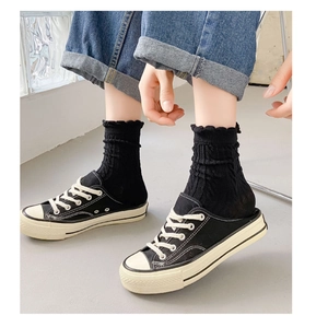 Detail showing black mid-calf socks with frilly edges paired with black canvas shoes