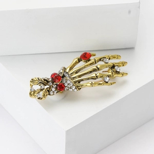 Vintage punk gold skeleton hand brooch with red and clear rhinestones on white background