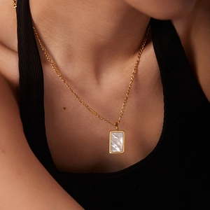 Close-up of a gold rectangle necklace with white shell inlay on a model neck